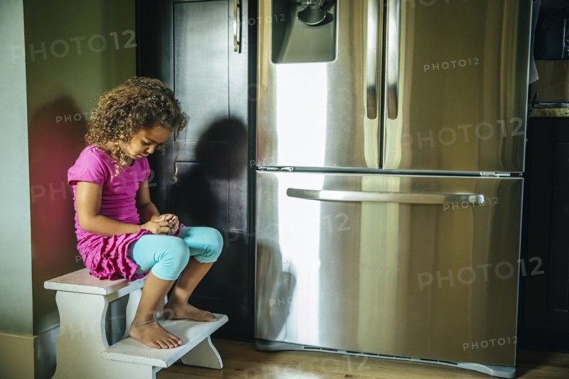 Sad mixed race girl sitting near refrigerator