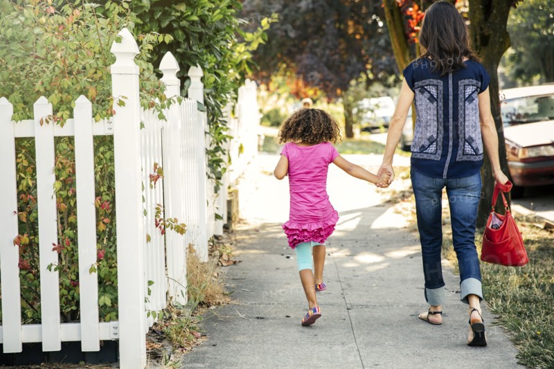 Mother and daughter holding hands on sidewalk