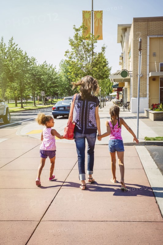 Mother and daughters holding hands on neighborhood sidewalk