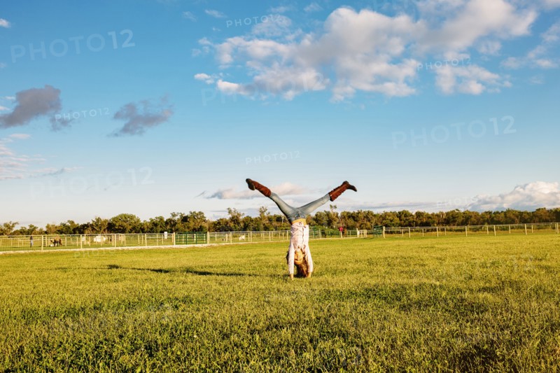 Caucasian girl doing headstand in field on ranch