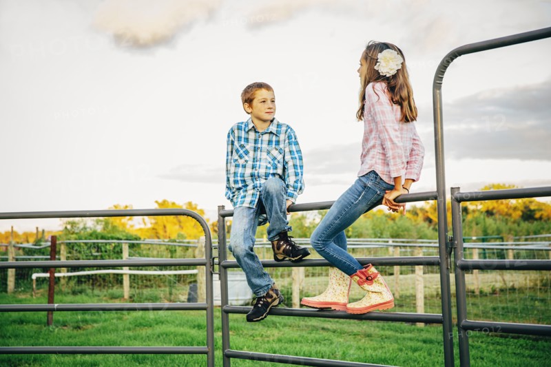 Caucasian children sitting on fence on farm