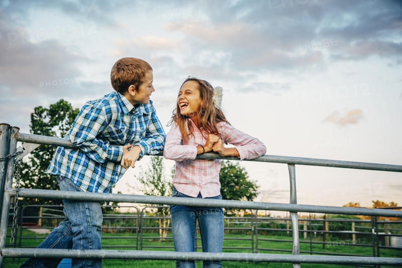 Caucasian children standing on fence on farm