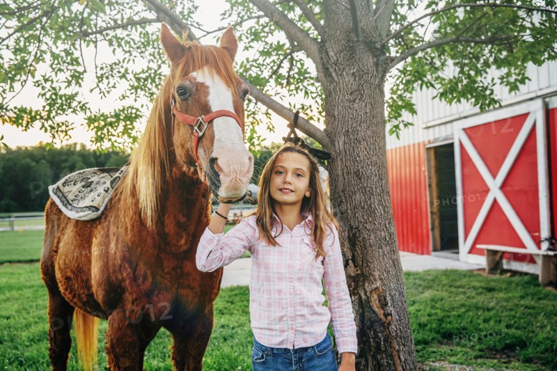 Caucasian girl walking horse outside barn on farm