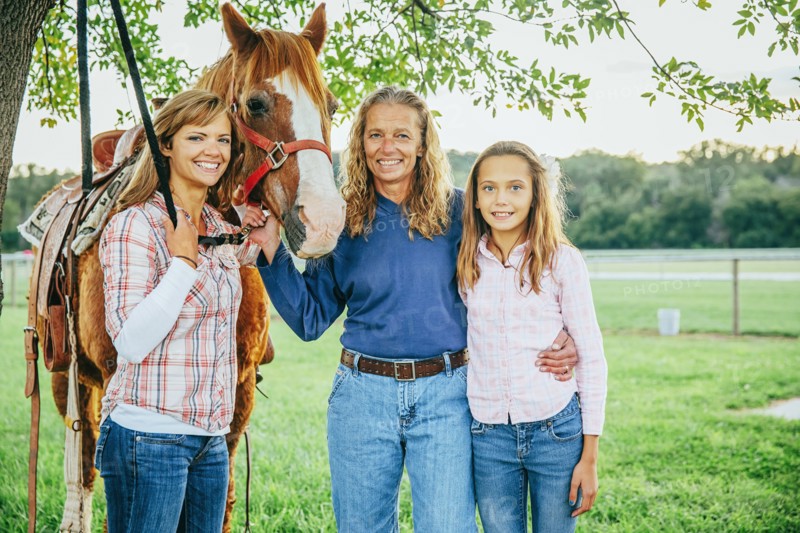 Three generations of Caucasian women standing near horse on farm