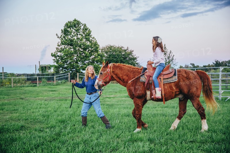Caucasian mother and daughter walking horse on ranch