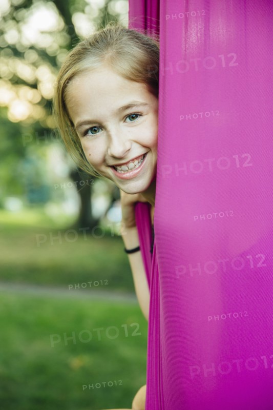 Acrobatic Caucasian girl sitting in hanging fabric