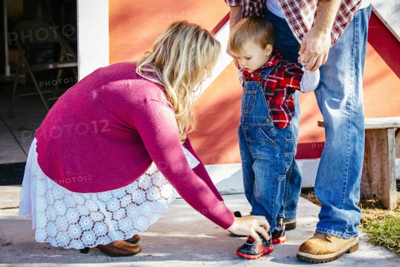 Caucasian mother tying shoes of son outside barn