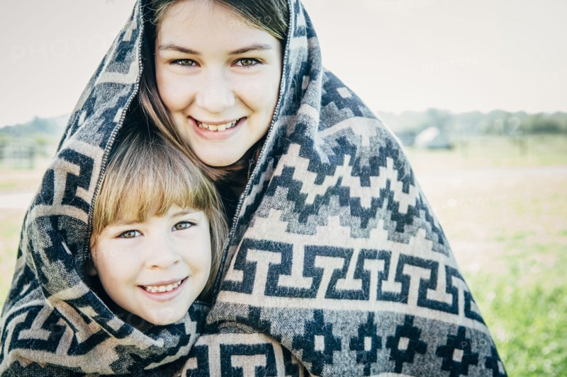Caucasian sisters wrapped in blanket on farm