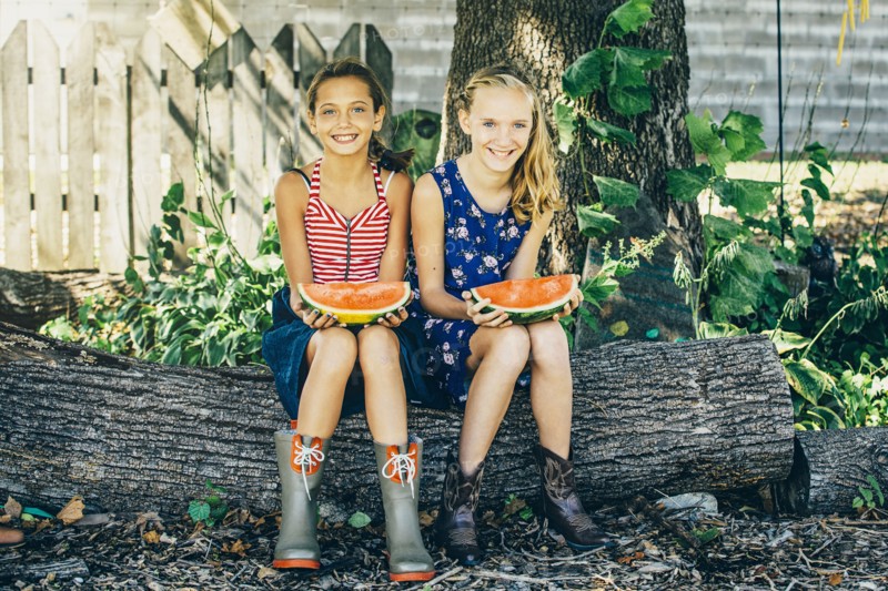 Caucasian girls eating watermelon under tree