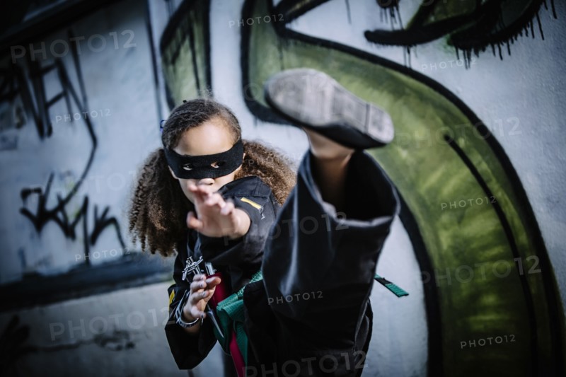 Mixed race girl kicking in martial arts uniform and mask