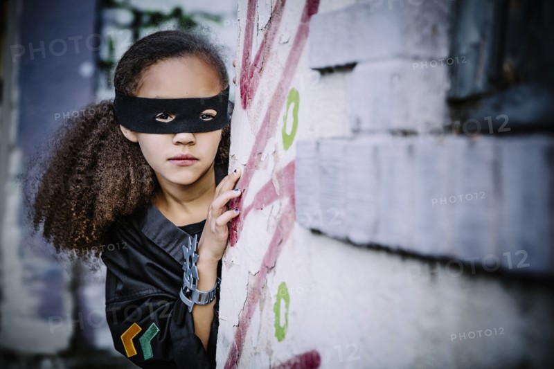 Mixed race girl in mask peeking around corner