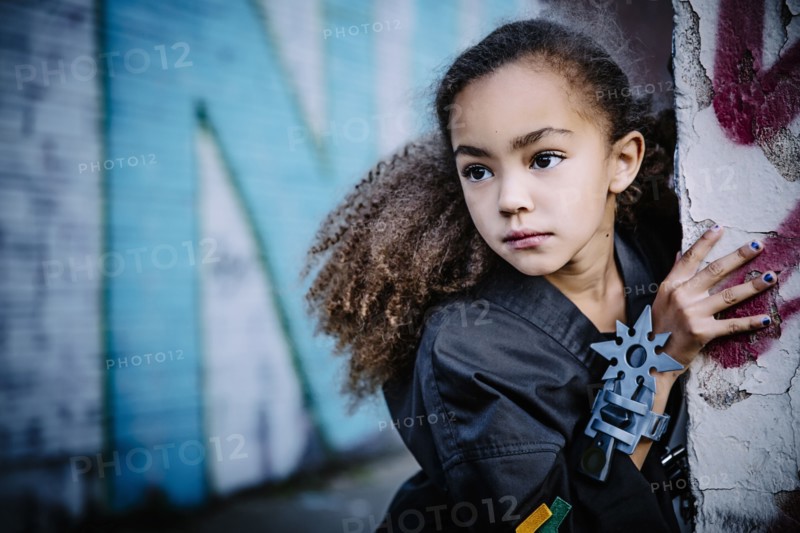 Mixed race girl in martial arts uniform with throwing star peeking around corner