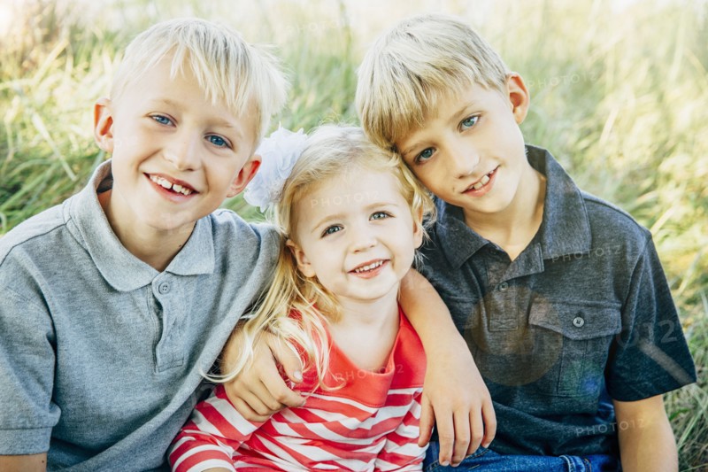 Caucasian brothers and sister smiling in grass