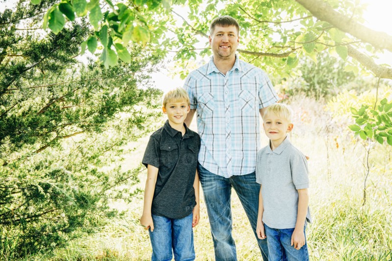 Caucasian father and sons smiling under trees