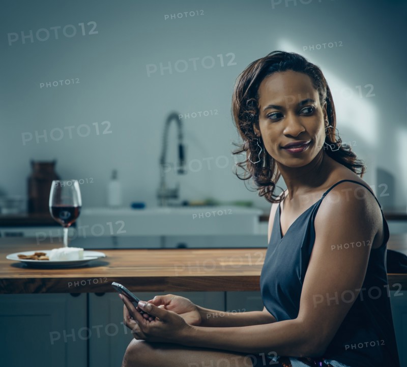 Black woman using cell phone at kitchen counter