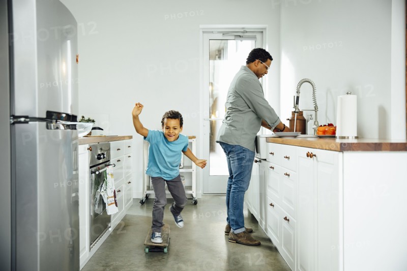 Boy skateboarding near father in kitchen