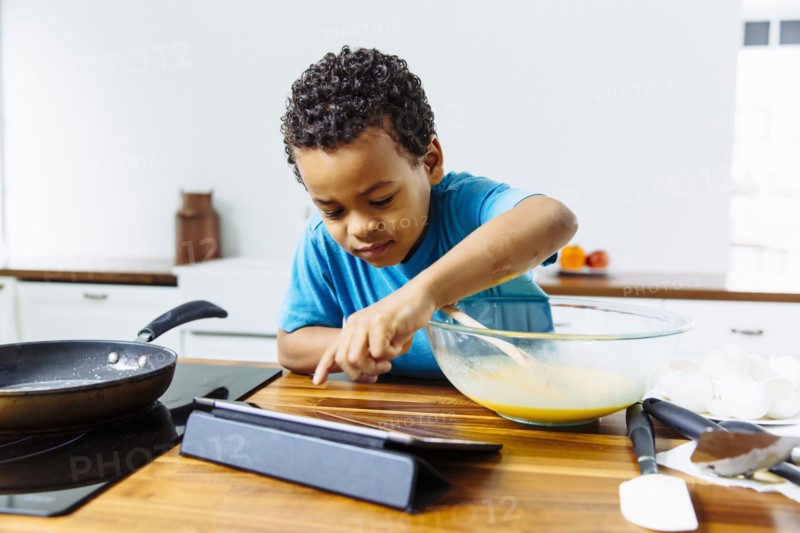 Mixed race boy cooking breakfast with digital tablet in kitchen