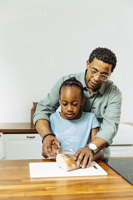 Father teaching daughter to slice bread in kitchen