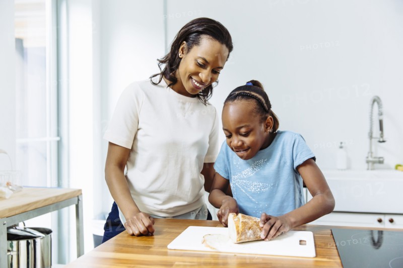Black mother and daughter slicing bread in kitchen