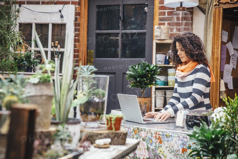 Mixed race employee using laptop in plant nursery