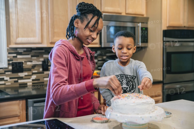 Black brother and sister decorating cake in kitchen