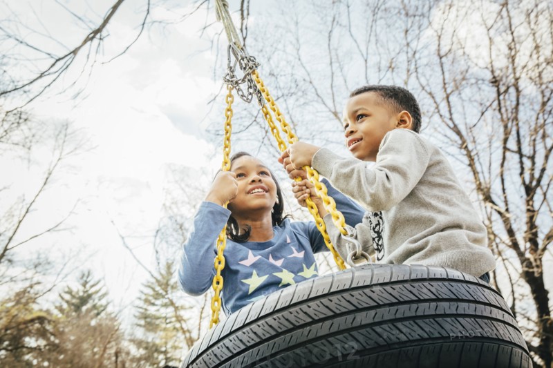 Black brother and sister playing on tire swing