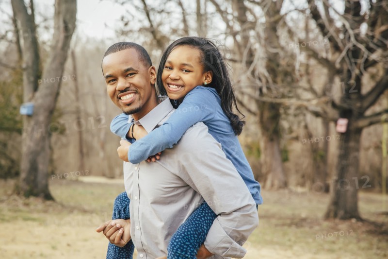 Black father carrying daughter piggyback outdoors