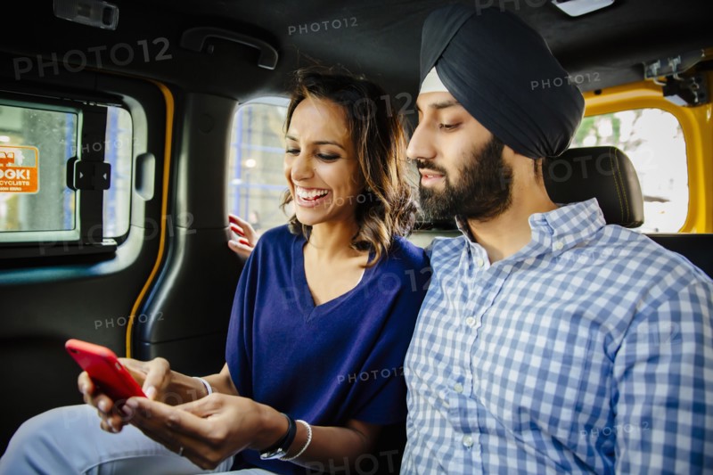 Indian couple using cell phone in taxi