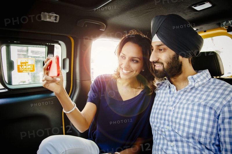 Indian couple taking selfie with cell phone in taxi