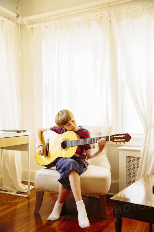 Caucasian boy playing guitar in living room