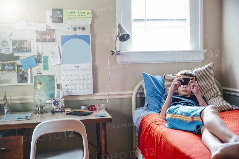 Caucasian boy using cell phone on bed
