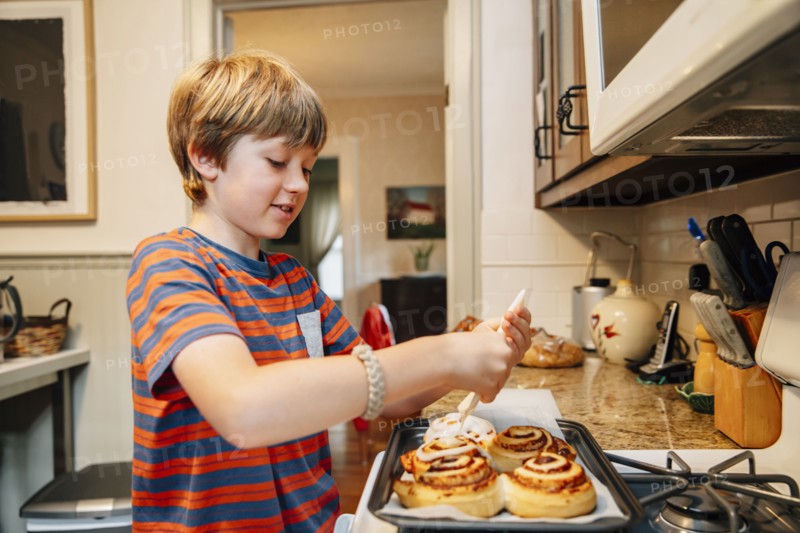 Caucasian boy frosting cinnamon rolls in kitchen