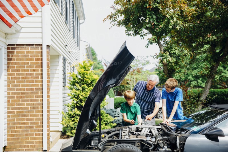 Caucasian grandfather and grandsons repairing car in driveway
