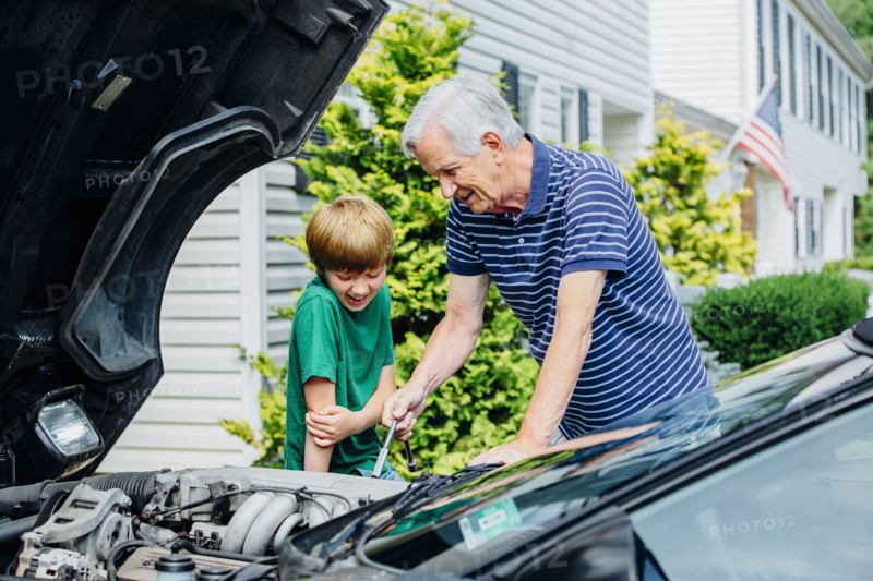 Caucasian grandfather and grandson working on car in driveway