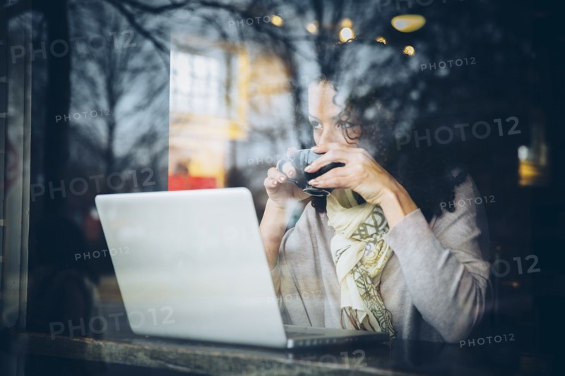 Mixed race woman drinking coffee and using laptop in cafe