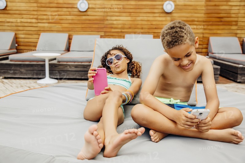 Mixed race children taking selfie with cell phones on patio