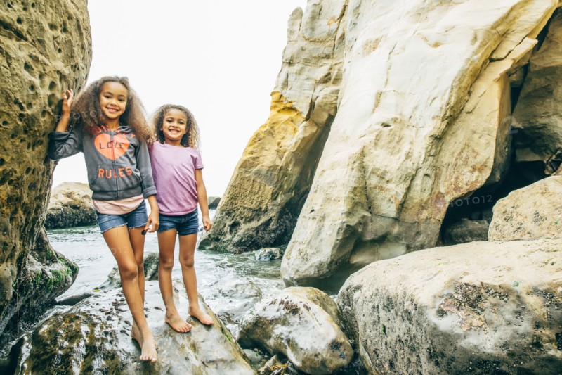 Mixed race sisters smiling on rocks