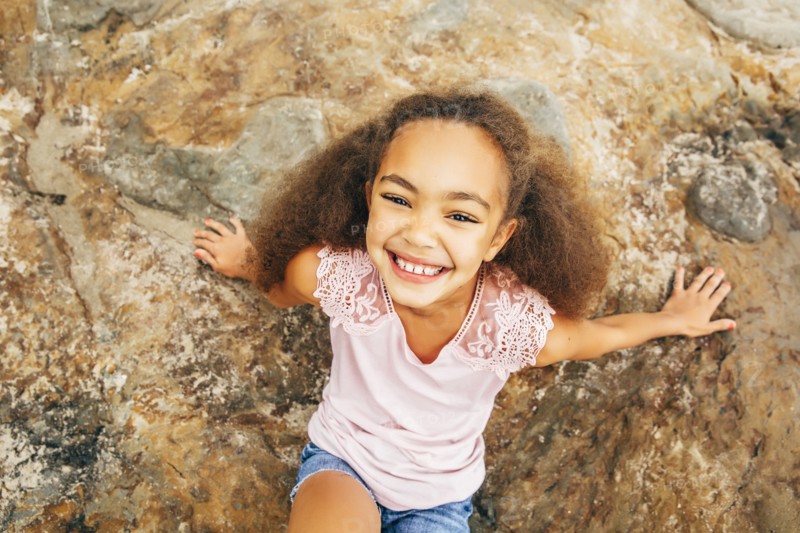Mixed race girl smiling on rock outdoors
