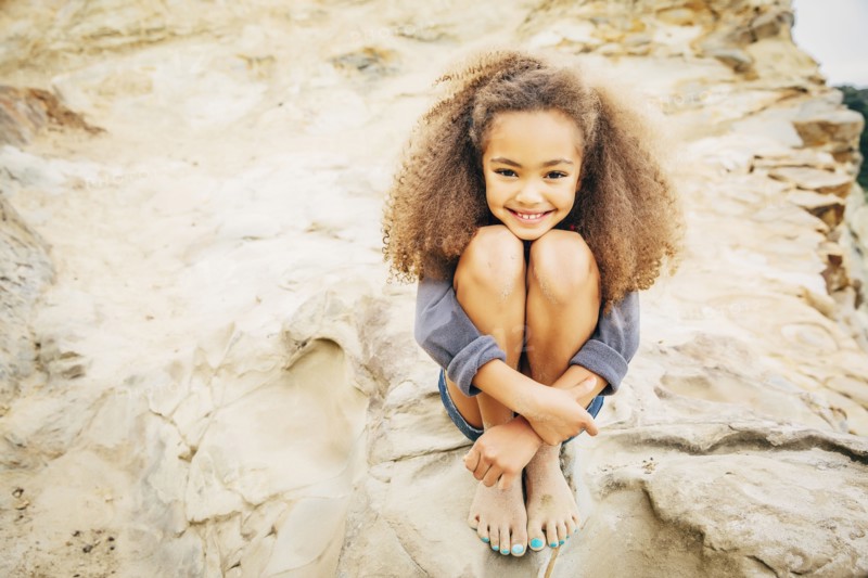 Mixed race girl hugging knees on rock