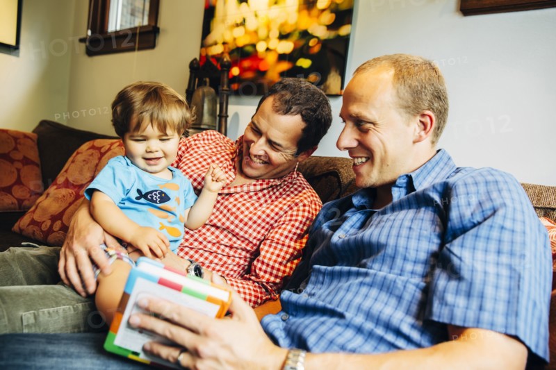 Gay fathers playing with baby son on sofa