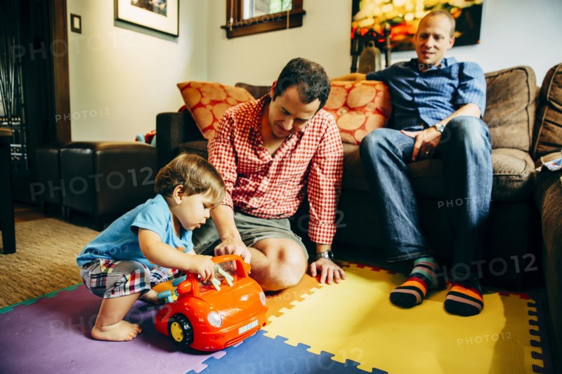 Gay fathers playing with baby son in living room