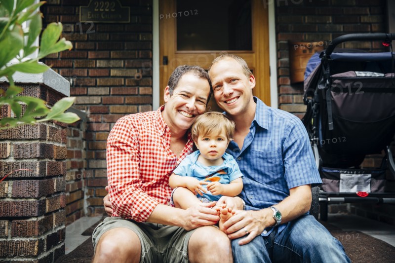Gay fathers holding baby son on front stoop