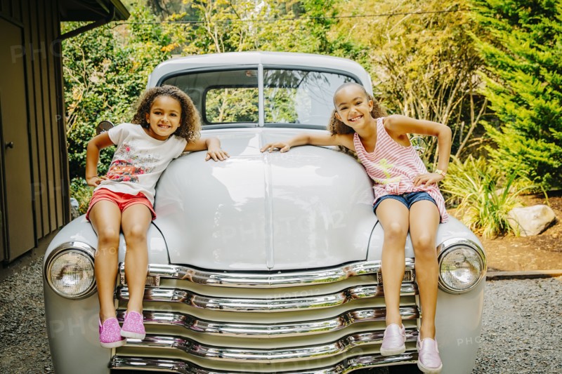 Mixed race sisters sitting on vintage car