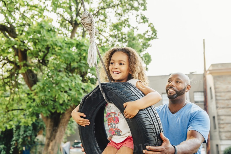 Father pushing daughter on tire swing