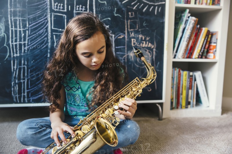 Mixed race girl playing saxophone on floor