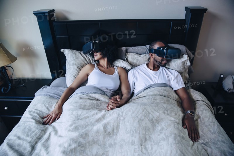 Couple using virtual reality goggles in bed