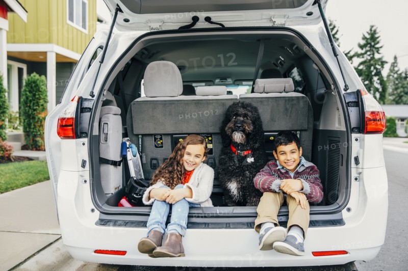 Mixed race children sitting with dog in car hatch