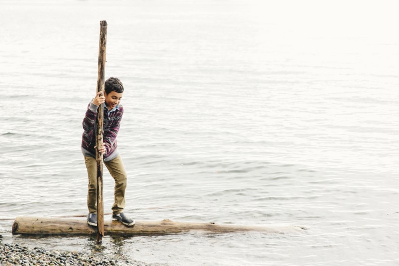 Mixed race boy playing on log in lake