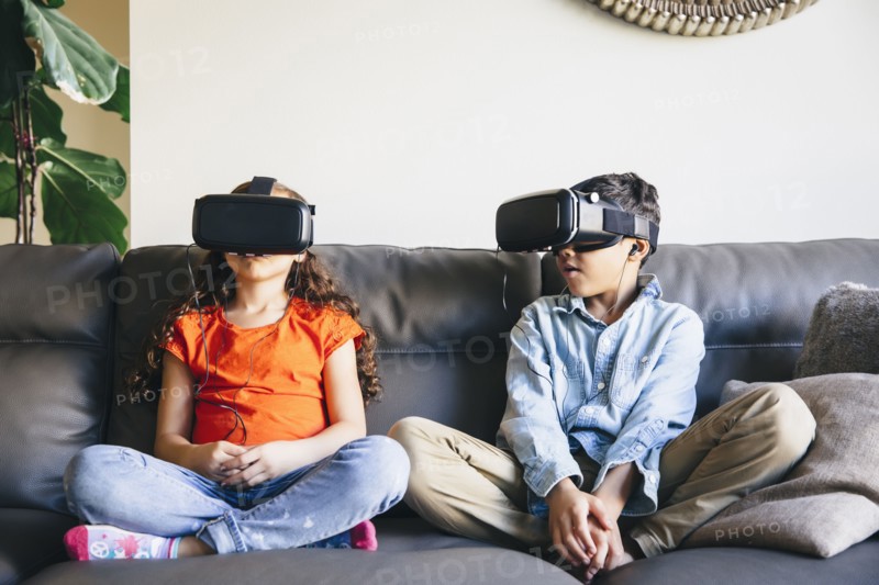 Mixed race children using virtual reality goggles on sofa