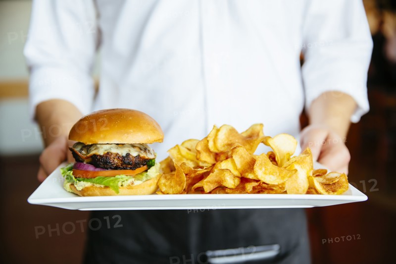 Caucasian waiter holding plate of cheeseburger and chips